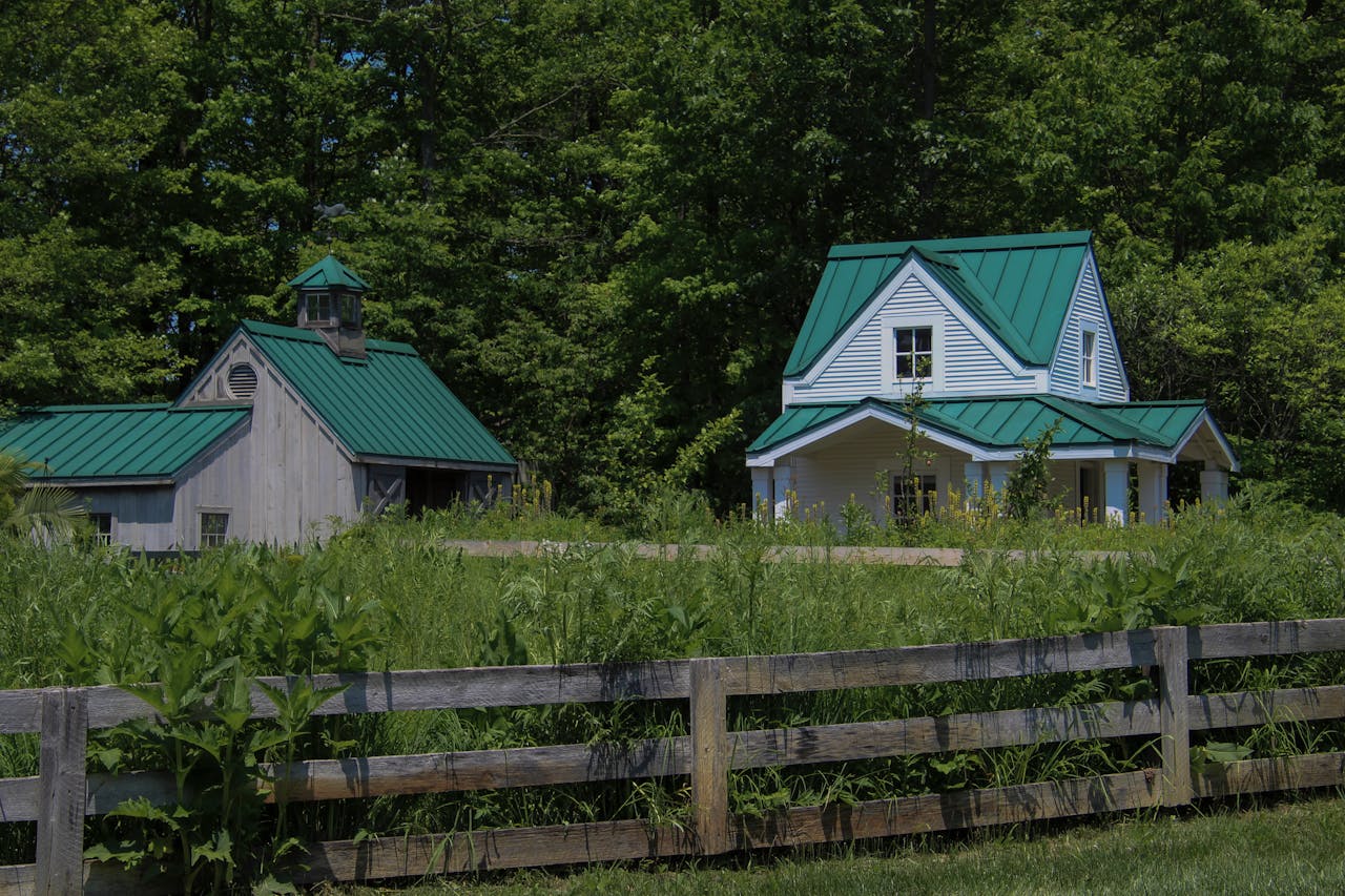 A picturesque rural scene featuring a charming house and barn with green roofs surrounded by lush greenery.