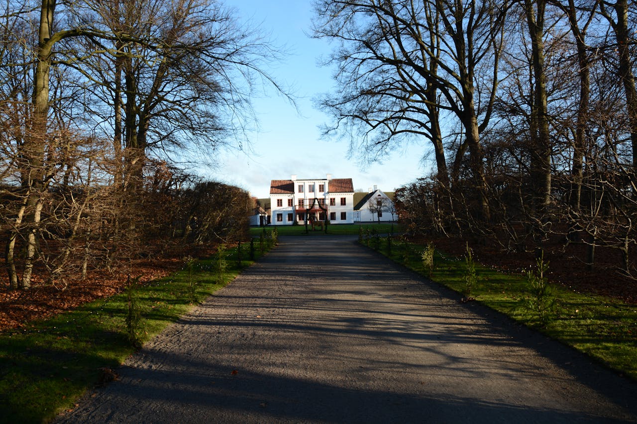 A quaint white house at the end of a tree-lined path, evoking a peaceful winter scene.